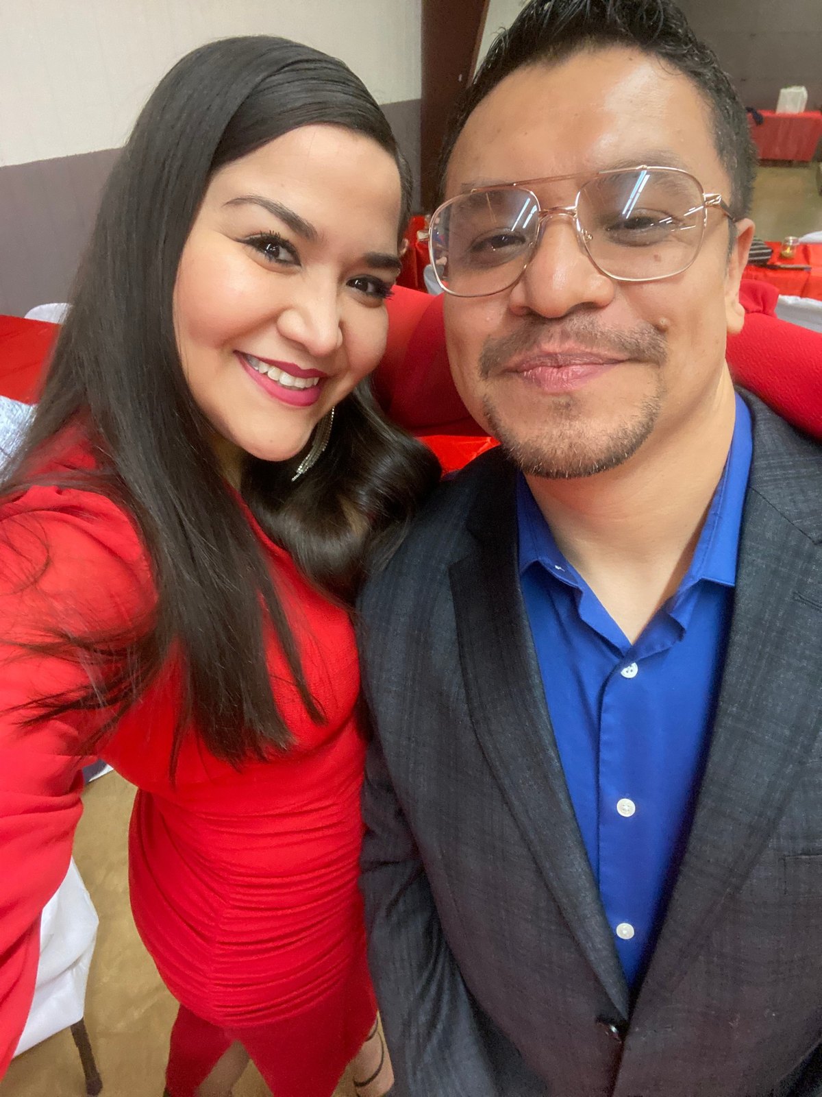 Azucena in red and Jesus in a blue shirt and glasses, smiling together in a close selfie