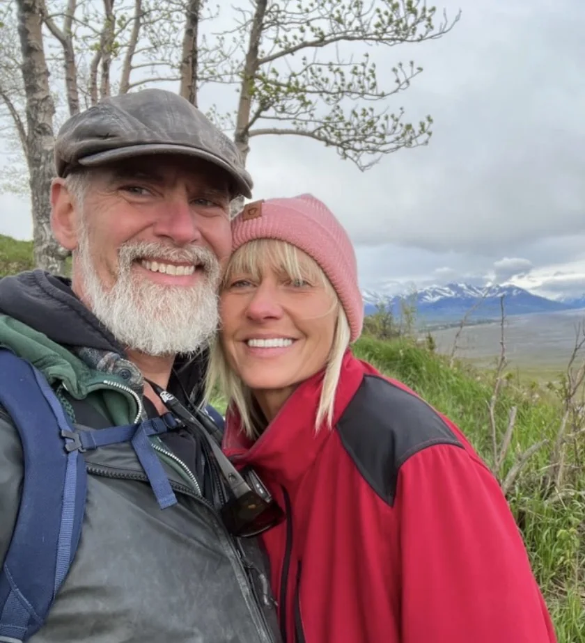 Wendy in a red jacket with her partner outdoors near the mountains