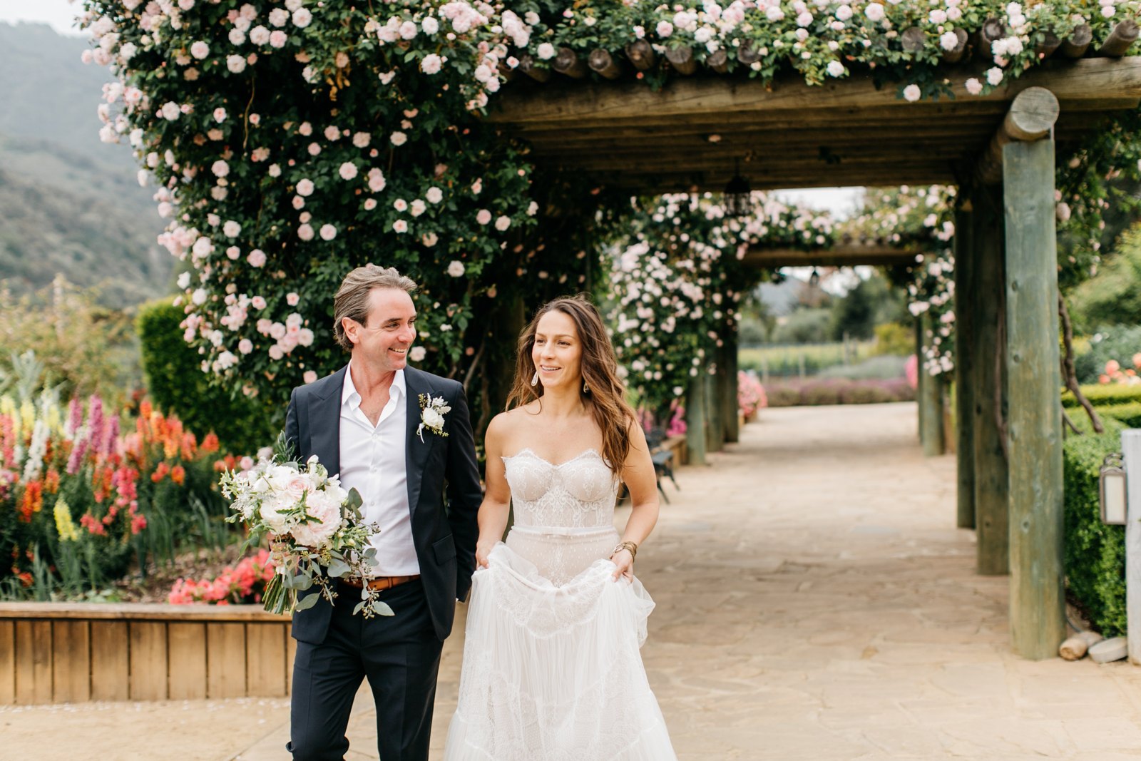 Jodi and Dennis walking beneath a flowering pergola on their wedding day