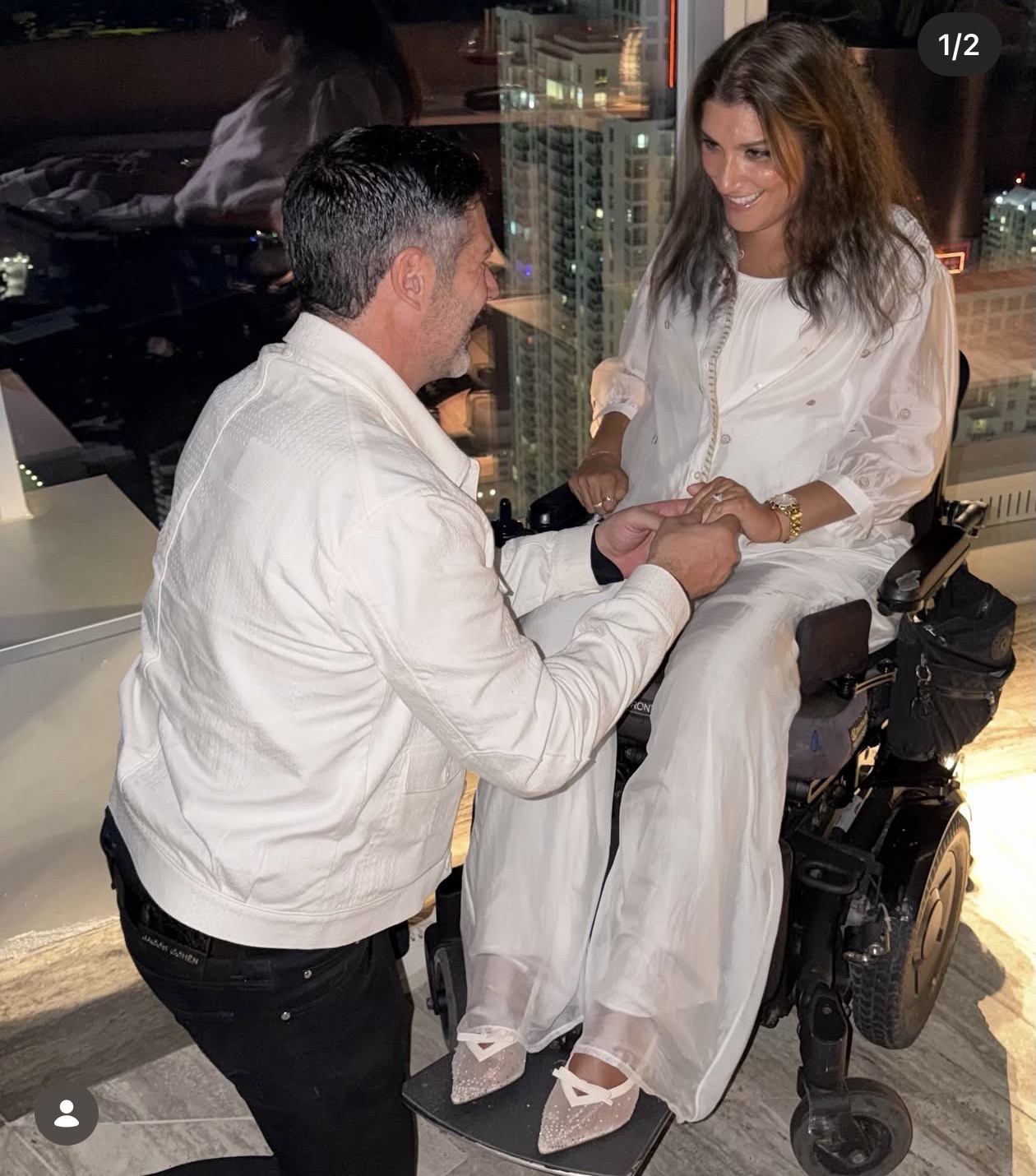 Sabrina seated in her wheelchair, smiling with Brian as he holds her hands