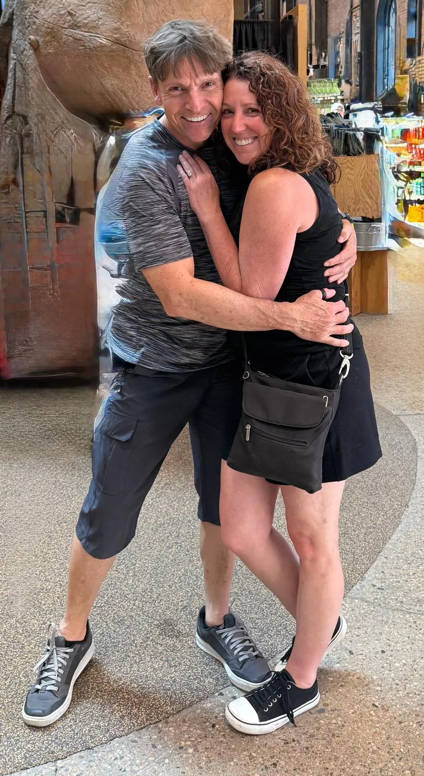 Aimee and Peter smiling as they embrace, his arms around her