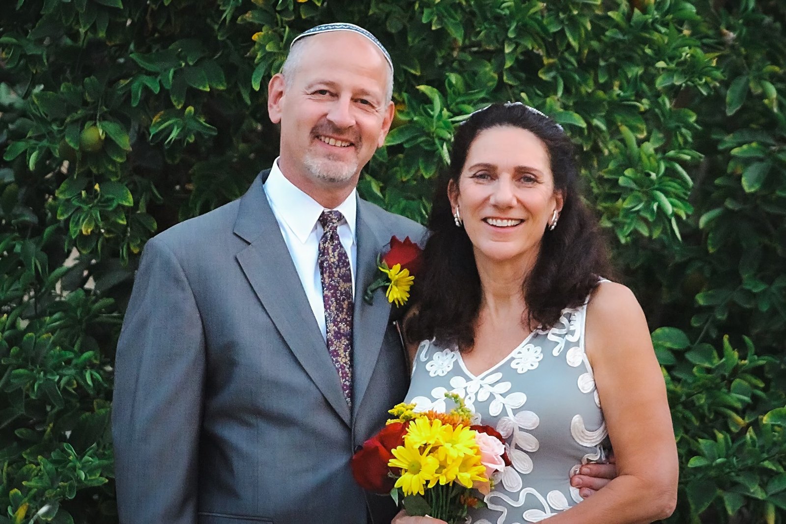 Pam and Ross smiling together outdoors, Pam holding a bouquet of sunflowers