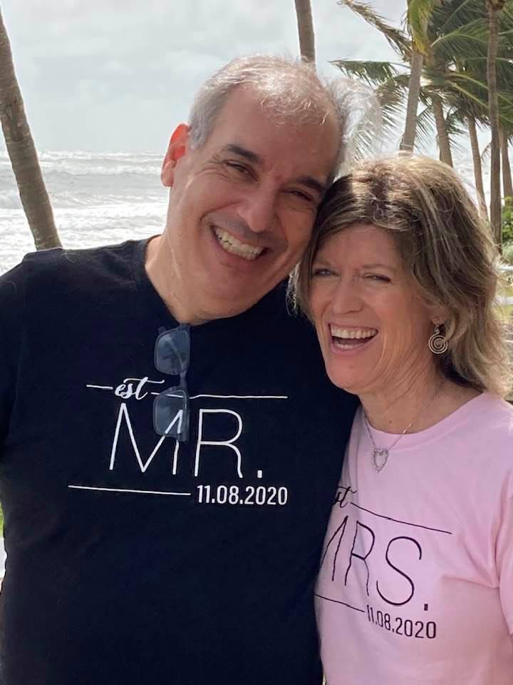 Melanie and Eric smiling at the beach in matching Mr. and Mrs. shirts